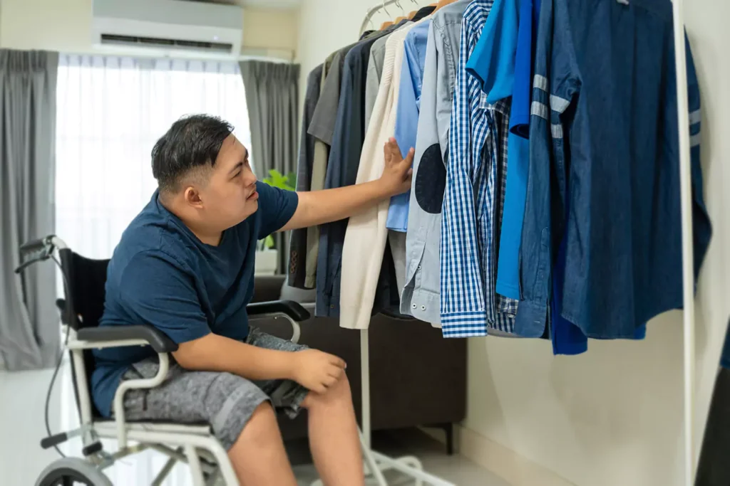 A young man with down syndrome is picking something to wear from his personal clothing
