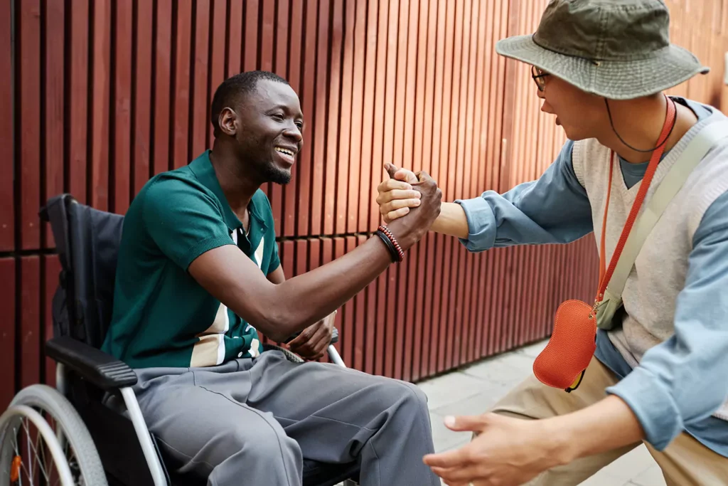 Two friends, one disabled are greeting each other happily outdoors