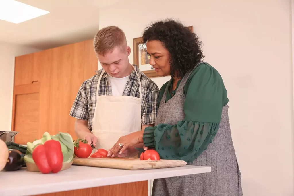 A young disabled man and his care giver are preparing vegetables in the kitchen for cooking