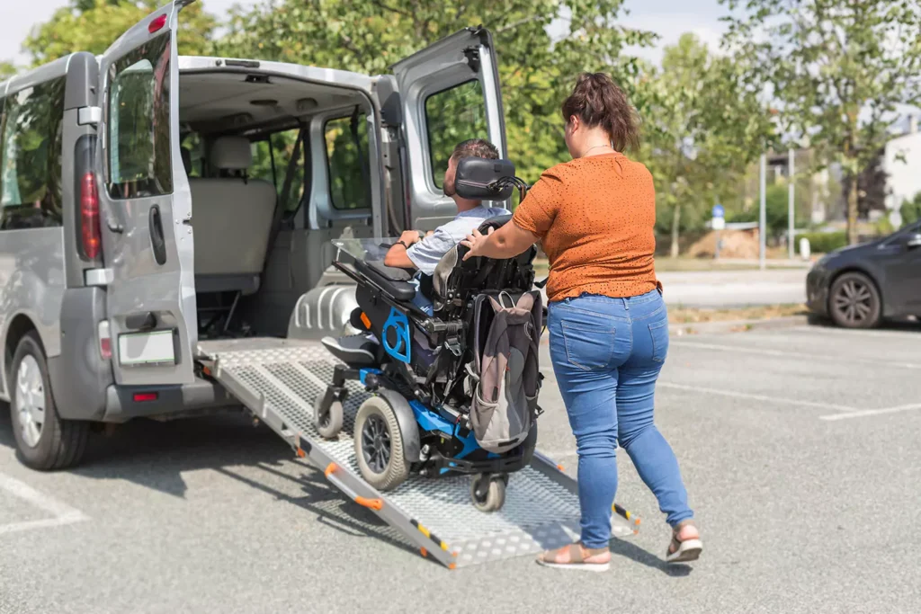 A support worker is assisting in pushing a disabled man in a wheelchair into a specialty disability vehicle