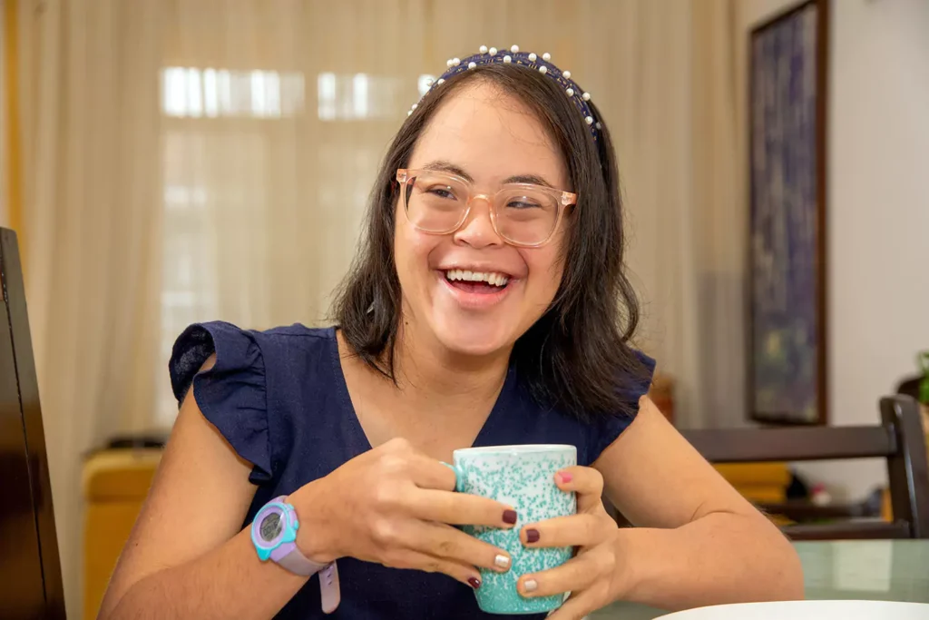A young woman with down syndrome is smiling while having a cup of coffee